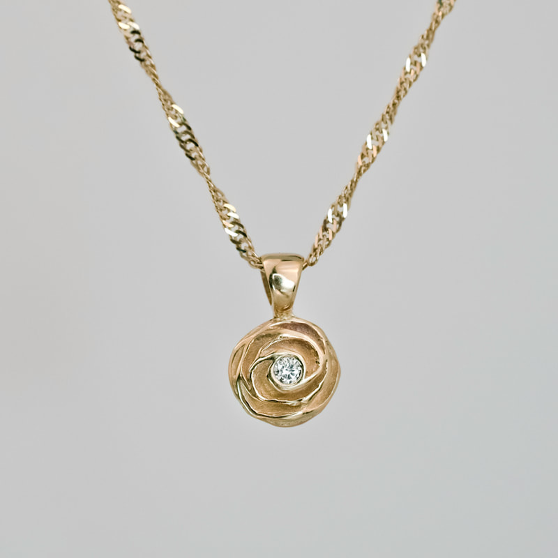 Hand carved rose flower pendant with a small gypsy set diamond in the center of the flower and a custom designed, attached bail, cast in 14K yellow gold.