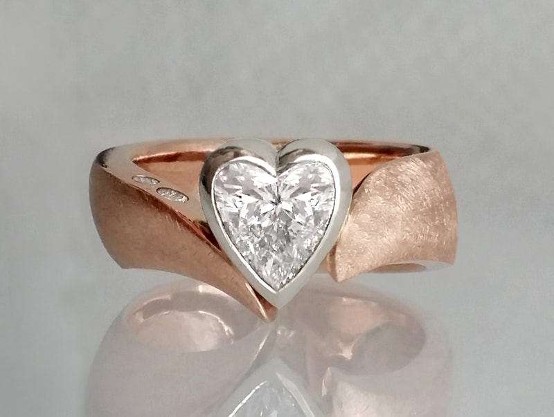 Modern heart diamond engagement ring set in a 14K white gold bezel setting and a 14K rose gold shank with two small diamonds placed on the side facet.