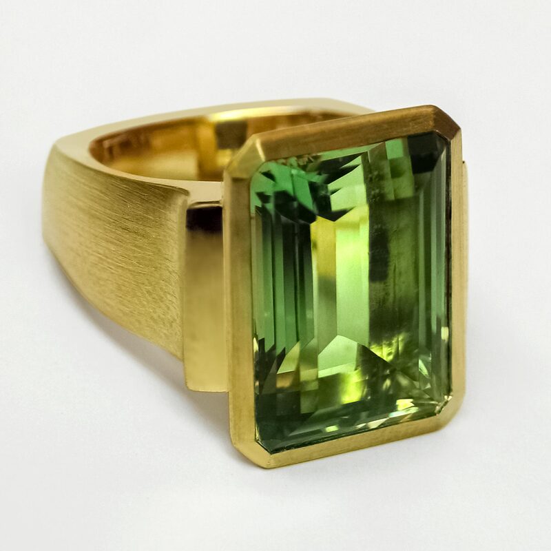 Large emerald cut green tourmaline, set in a heavy Euro shank bezel setting in 18K yellow gold with slits on the sides to let in light.