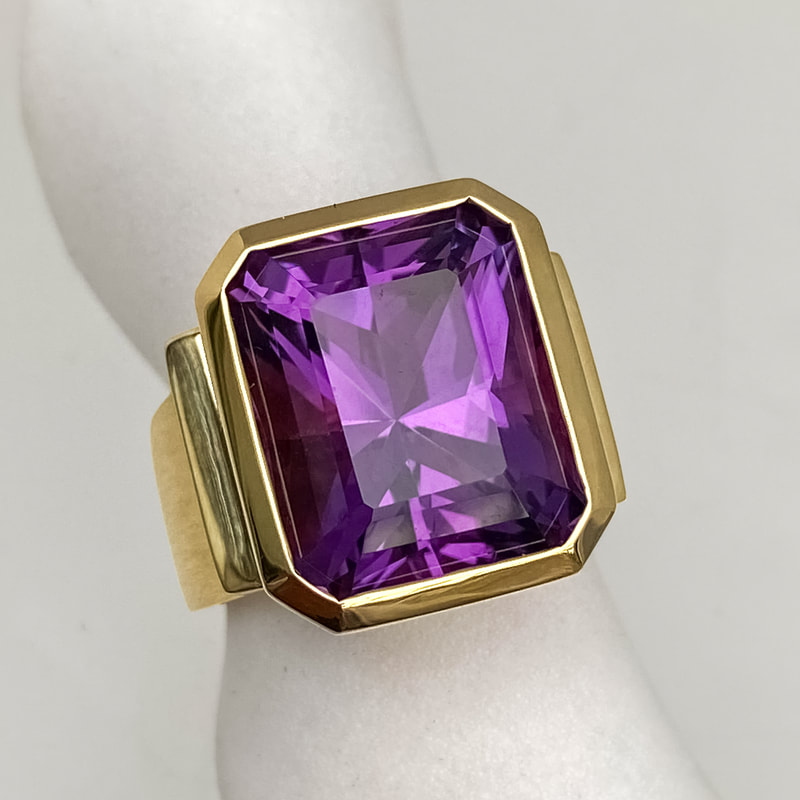 Large emerald cut natural amethyst set in a heavy Euro shank bezel setting in 18K yellow gold with slits on the sides to let in light.